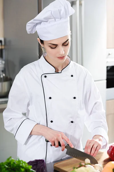 Chef femenino profesional que corta ingredientes por el mostrador de cocina - foto de stock