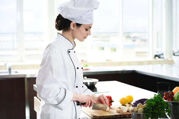 Chef femenino profesional que corta ingredientes para el plato - foto de stock