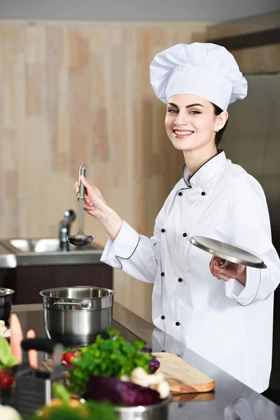 Professional female cook holding ladle by stove with pot — Stock Photo