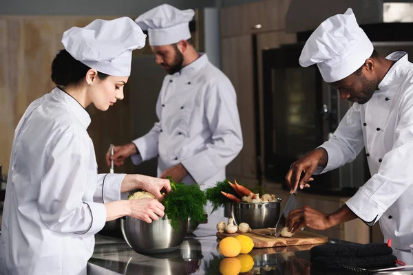 Multiracial team of cooks cooking by kitchen stove in restaurant — Stock Photo