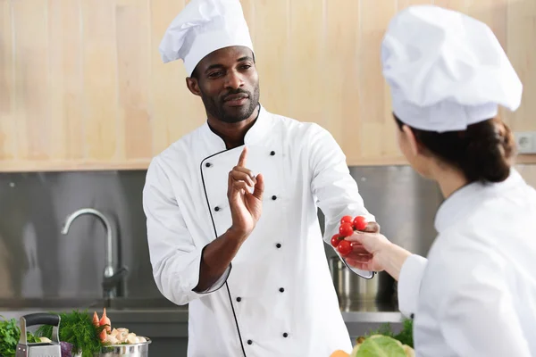 African american chef and female cook sharing cooking ingredients on kitchen — Stock Photo