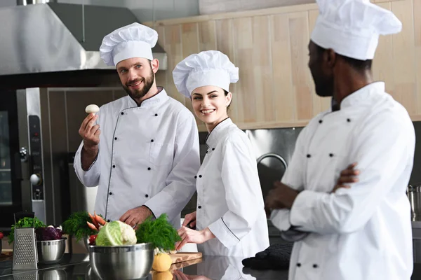 Equipo multirracial de cocineros que eligen ingredientes de cocina en la cocina moderna - foto de stock