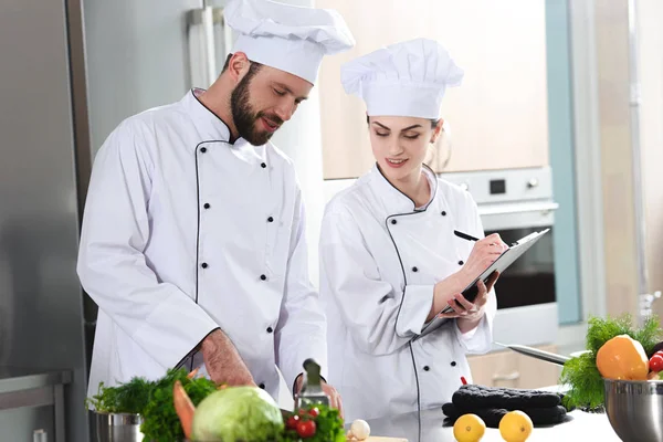 Equipe profissional de cozinheiros verificando a receita durante o prato de cozinha — Fotografia de Stock