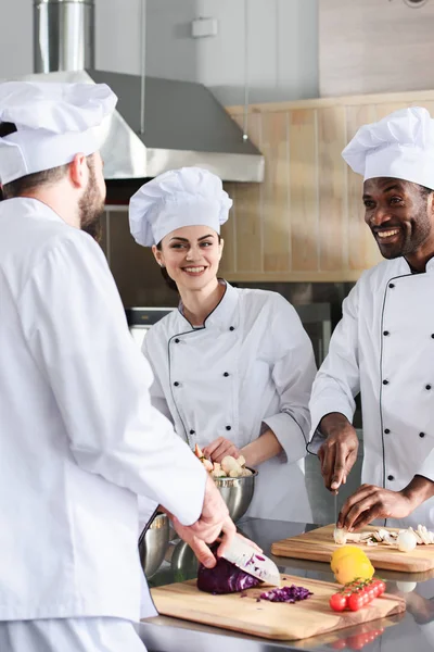 Equipe de chefs multirraciais sorrindo e cozinhando na cozinha moderna — Fotografia de Stock