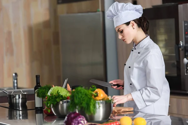 Chef femenino profesional que corta ingredientes en la mesa de la cocina - foto de stock