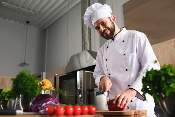 Cocinero masculino profesional cortando pimienta en la mesa de cocina - foto de stock