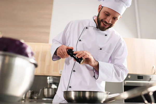 Prato de tempero de chef sorridente por fogão de cozinha — Fotografia de Stock