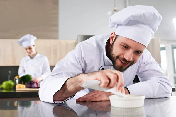 Männlicher Koch garniert Gericht auf Restaurantküche vor Köchin — Stockfoto