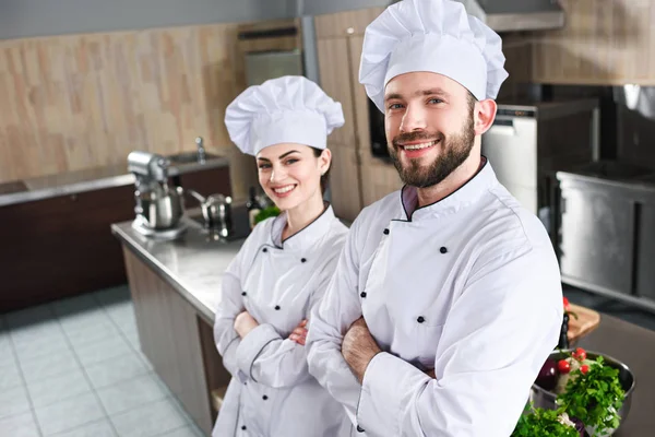 Professional team of male and female cooks standing with folded arms on kitchen — Stock Photo