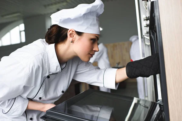 Woman cook checking baking oven in restaurant kitchen — Stock Photo