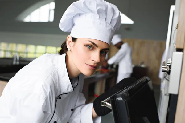 Mujer chef chequeando horno para hornear por el cocinero afroamericano en la cocina - foto de stock