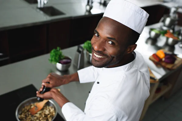 Sorrindo prato de tempero cozinheiro afro-americano pelo fogão de cozinha — Fotografia de Stock