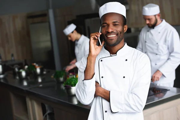 Chef afro-americano sorridente che parla con lo smartphone alla cucina del ristorante — Foto stock