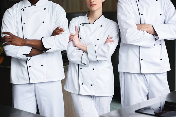 Cropped image of multicultural chefs standing with crossed arms at restaurant kitchen — Stock Photo