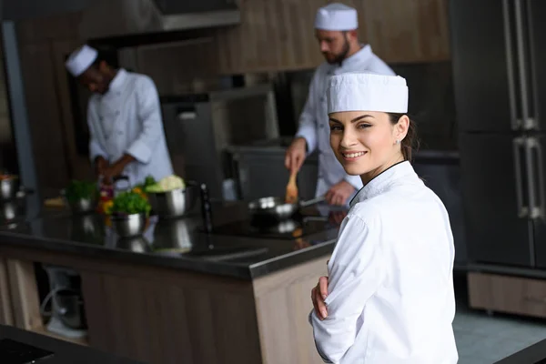 Sonriente hermoso chef mirando a la cámara en la cocina del restaurante - foto de stock