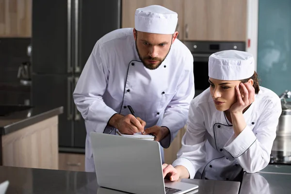 Chefs masculins et féminins utilisant un ordinateur portable à la cuisine du restaurant — Photo de stock