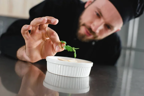 Chef bonito adicionando salsa ao prato na cozinha do restaurante — Fotografia de Stock