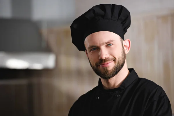 Portrait of handsome chef in black uniform looking at camera at restaurant kitchen — Stock Photo