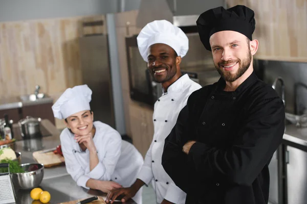 Chef multiculturali sorridenti che guardano la macchina fotografica alla cucina del ristorante — Foto stock