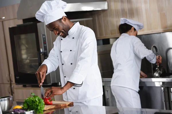 Chef afroamericano corte pimiento en la cocina del restaurante - foto de stock