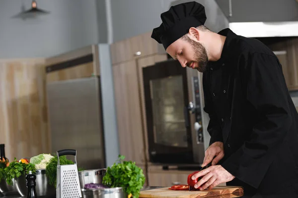 Vue latérale du beau chef coupant le poivron au restaurant cuisine — Photo de stock