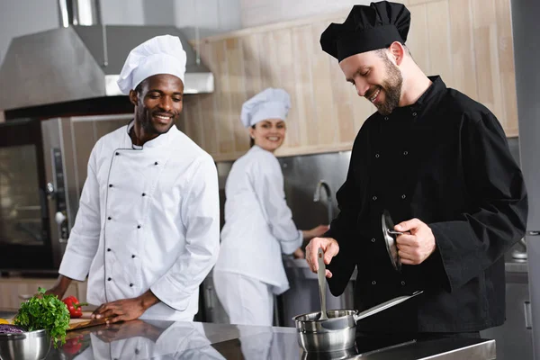 Chefs multiculturales sonrientes cocinando juntos en la cocina del restaurante - foto de stock