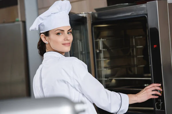 Atractivo chef de pie cerca del horno en la cocina del restaurante - foto de stock