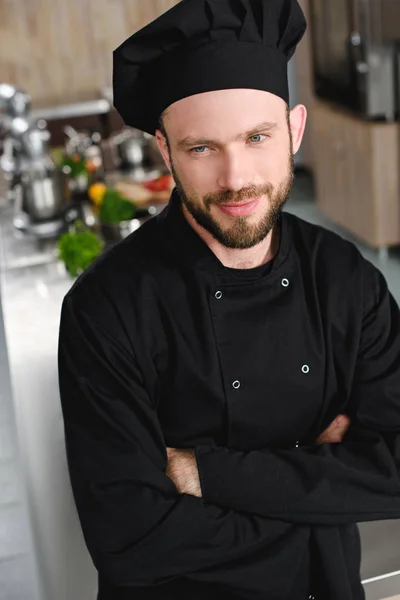 Handsome chef standing with crossed arms and looking away at restaurant kitchen — Stock Photo