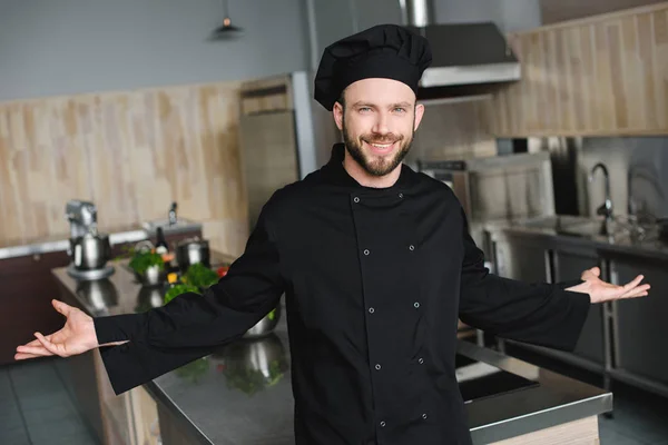 Sonriente guapo chef de pie con los brazos abiertos en la cocina del restaurante - foto de stock