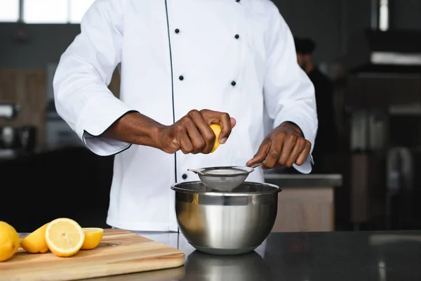 Imagen recortada del chef afroamericano exprimiendo limones en la cocina del restaurante - foto de stock