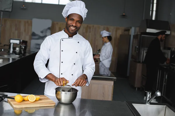 Улыбающийся красивый африканский шеф-повар, выжимающий лимоны на кухне ресторана — стоковое фото