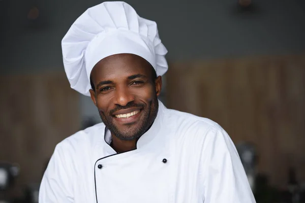 Retrato del guapo chef afroamericano mirando a la cámara en la cocina del restaurante - foto de stock