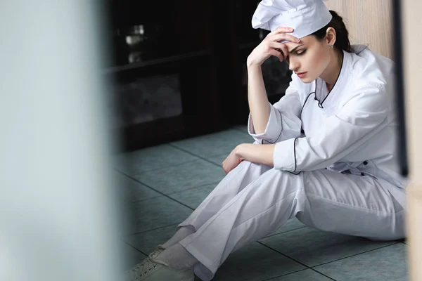 Triste chef sentado en el piso en la cocina del restaurante - foto de stock