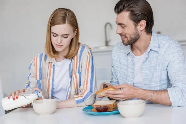 Joven mujer verter en bowl y novio difusión mermelada en tostadas - foto de stock