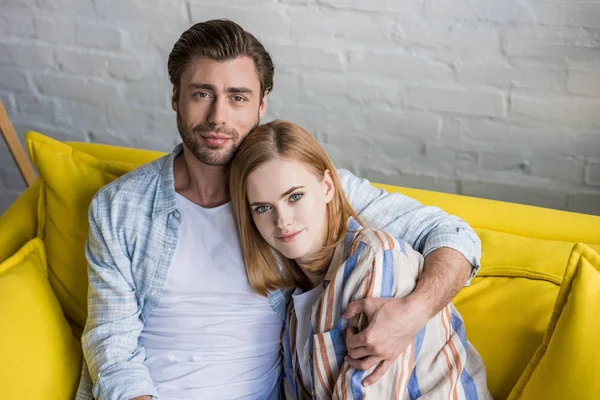 Retrato de pareja joven con estilo sentado en el sofá delante de la pared de ladrillo - foto de stock