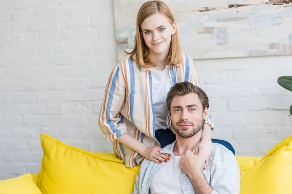 Smiling young woman sitting on edge of couch and embracing boyfriend — Stock Photo
