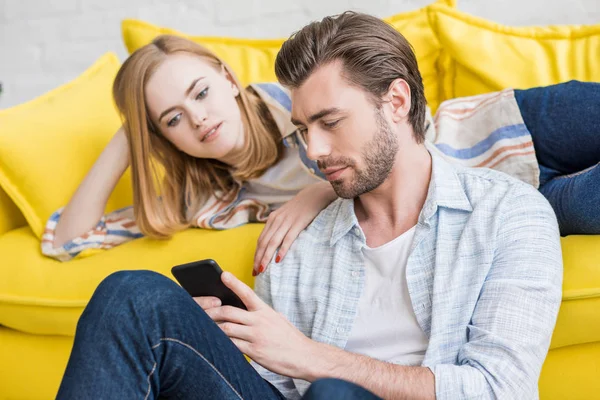 Молода жінка лежить на дивані і дивиться хлопець за допомогою смартфона — стокове фото