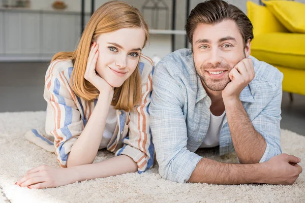 Joven sonriente pareja tendida en la alfombra en sala de estar - foto de stock