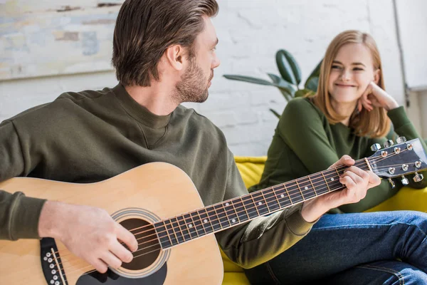 Joven con estilo tocando en la guitarra acústica a la novia sonriente - foto de stock