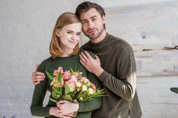 Vorderansicht einer stilvollen jungen Frau mit Blumen und einem Freund, der sie umarmt — Stockfoto