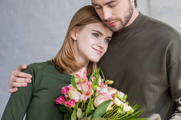 Jeune femme souriante avec des fleurs sur l'épaule du petit ami — Photo de stock