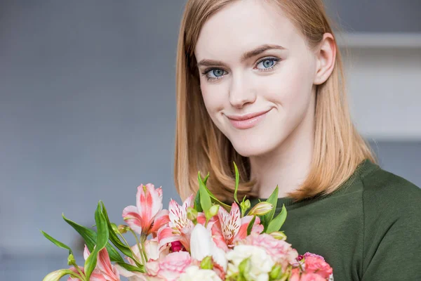 Portrait of young smiling woman holding bouquet of flowers — Stock Photo