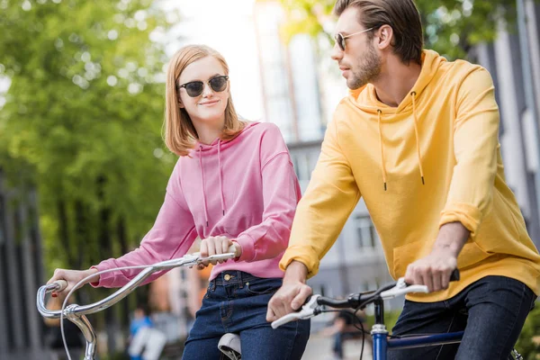 Elegante pareja joven en gafas de sol a caballo en bicicletas - foto de stock