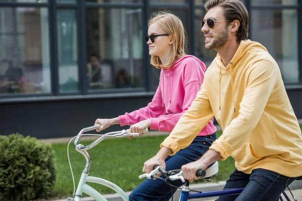 Side view of stylish couple in sunglasses riding on bicycles — Stock Photo