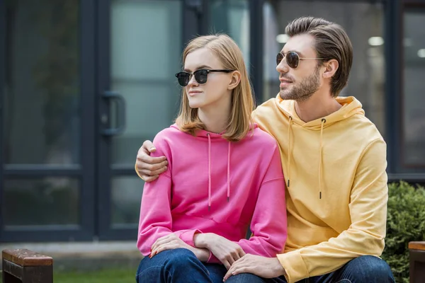 Young stylish man embracing girlfriend on bench — Stock Photo