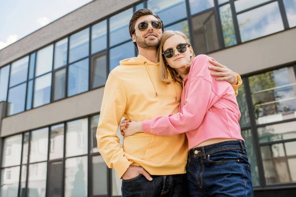 Low angle view of young stylish woman in sunglasses embracing boyfriend — Stock Photo