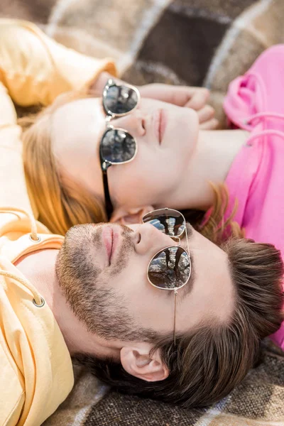 Stylish young couple in sunglasses laying on woolen plaid — Stock Photo
