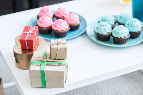Cupcakes rosas y azules y cajas de regalo en mesa blanca, concepto de fiesta de bebé - foto de stock
