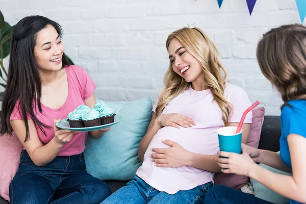 Мультикультурні жінки пропонують вагітному другу кекси і пити під час дитячої вечірки — стокове фото
