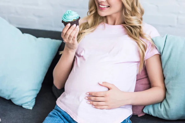 Imagem cortada de mulher grávida segurando cupcake e tocando barriga na festa do bebê — Fotografia de Stock